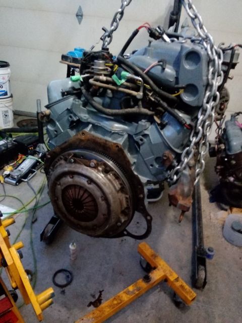 1994 Ford Bronco - Engine assembly suspended by chains, with a clutch visible, in a garage setting.