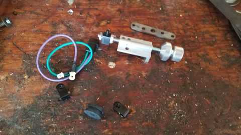 1985 Ford Bronco - Various automotive parts and hardware are scattered on a workbench, including electrical connectors and a metal assembly.