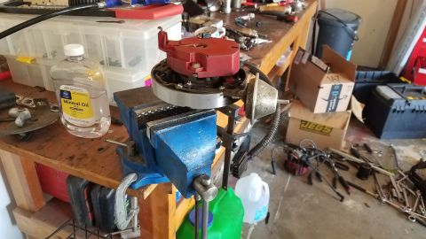 1985 Ford Bronco - A distributor is clamped in a vise on a wooden workbench, surrounded by various tools and a bottle of mineral oil.
