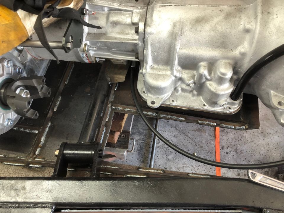 Close-up of a vehicle's transmission housing, driveshaft yoke, and frame components during assembly or repair