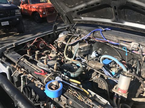 1989 Ford Bronco - The engine bay of a vehicle is shown with various tools and parts. Another truck is parked nearby.