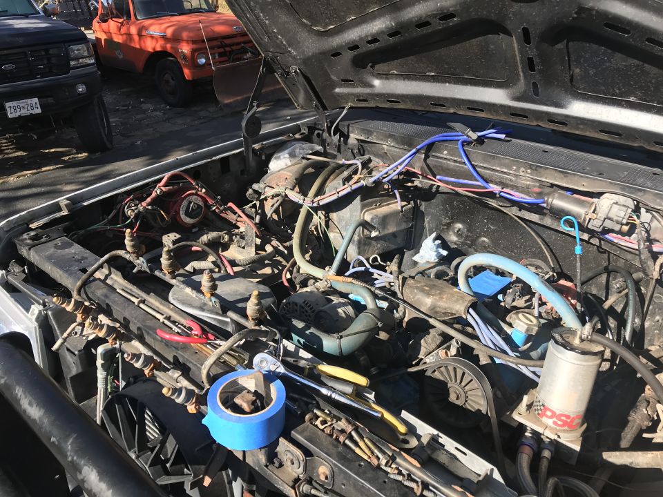 Engine bay with tools and tape, two trucks in background