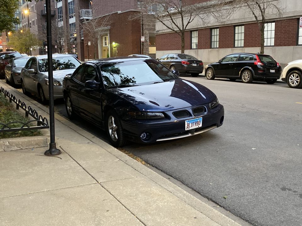 Dark blue 2000 Pontiac Grand Prix coupe parked curbside, front 3/4 view. License plate reads BLUTRBQ