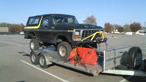 1978 Ford Bronco - A lifted black 1978 Ford Bronco with yellow trim is transported on a trailer, carrying a red snowblower.