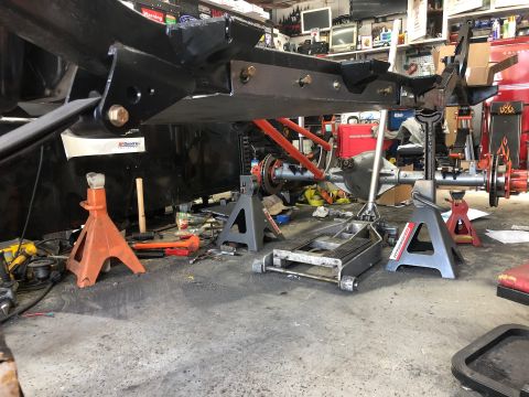 1992 Jeep Wrangler - The frame and suspension components of a vehicle are supported by jack stands in a workshop environment.