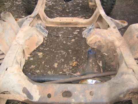 1978 Ford Bronco - The underside of a vehicle frame shows rust and dirt, with a differential and driveshaft exposed.