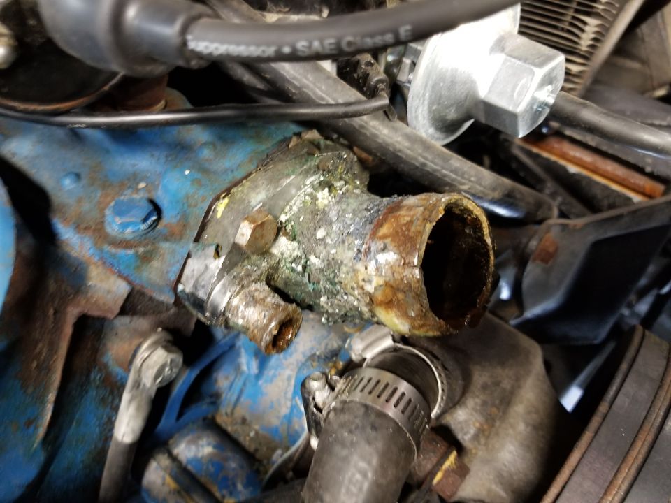 Corroded engine water outlet with rusted pipe and mineral deposits