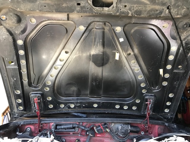 Underside of black car hood with red engine components visible below