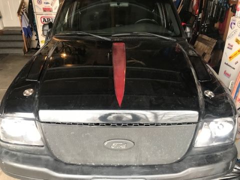 2000 Ford Explorer - A black Ford Ranger truck is parked in a garage, showing its front grille and hood with a red accent.