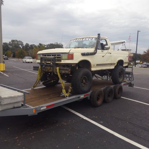 1988 Ford Bronco - This heavily modified pickup truck, possibly a 1987 model, is secured to a trailer for transport.