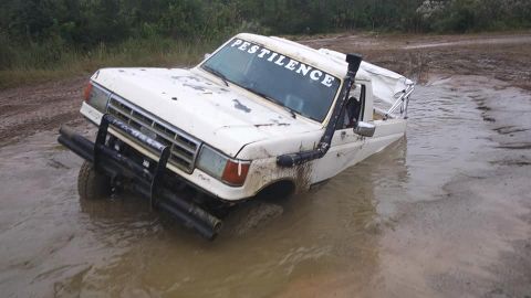 1988 Ford Bronco - White pickup truck stuck in mud with a snorkel and brush guard.