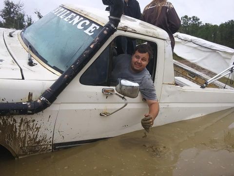 1988 Ford Bronco - A white pickup truck, modified with a snorkel, is submerged in mud with a driver visible through the window.