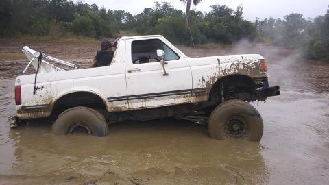 1988 Ford Bronco - A white Ford Bronco is stuck deep in the mud, with steam rising around it.
