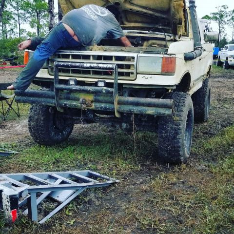 1988 Ford Bronco - Person working on engine of lifted 1987 Ford F-Series truck with aftermarket bumper and snorkel.