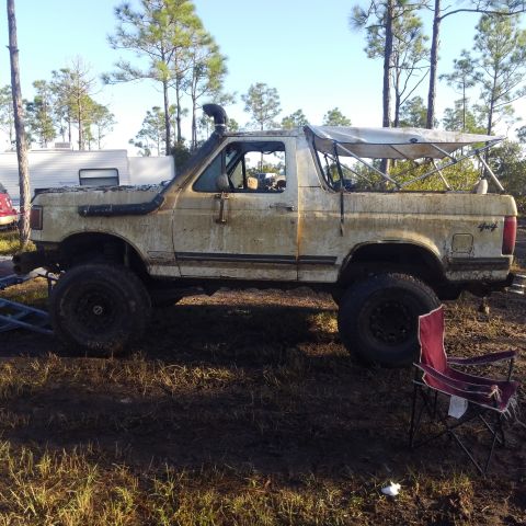 1988 Ford Bronco - A heavily modified Ford Bronco sits in a muddy outdoor area, equipped with off-road enhancements.
