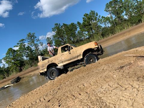 1988 Ford Bronco - Muddy 1987 Ford F-150 pickup truck navigating a water and mud obstacle course.