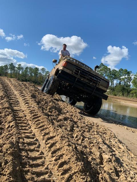 1988 Ford Bronco - A man sits atop a tan 1987 Ford Bronco as it navigates a muddy track at a park.