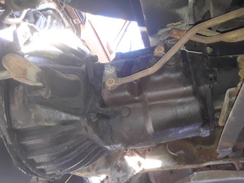 1994 Ford Bronco - This image shows the underside of a vehicle's transmission and drivetrain, with various metal parts and fluid residue visible.