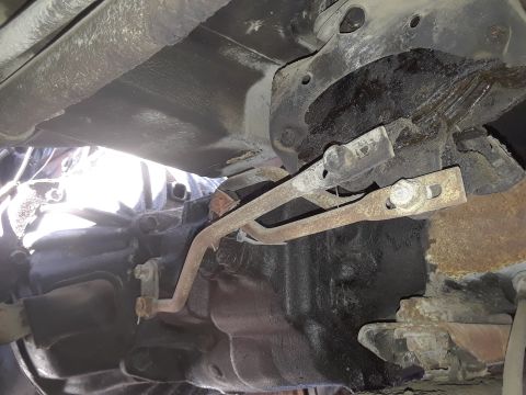 1994 Ford Bronco - Underside view of vehicle transmission and linkage components, showing rusty metal rods.
