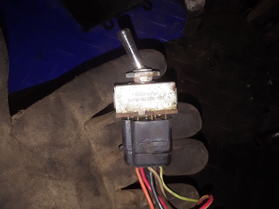 Gloved hand holding a toggle switch with a black connector and wires