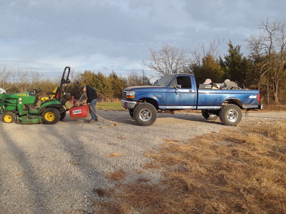 Blue pickup truck with lifted suspension and large tires, parked next to a green tractor