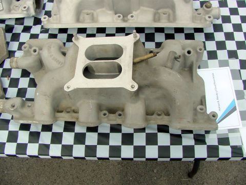 1969 Ford Mustang - An aluminum intake manifold is displayed on a checkered surface, with a document visible to the right.