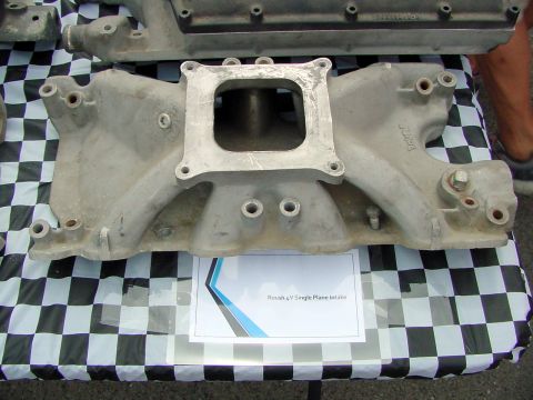 1969 Ford Mustang - A metal engine intake manifold is displayed on a checkered tablecloth, with text identifying it as a Roush part.