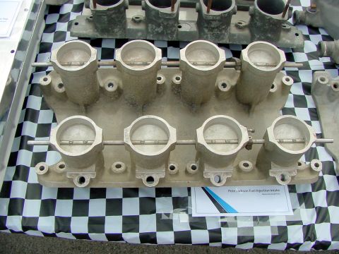 1969 Ford Mustang - A dual quad throttle body intake manifold, labeled as "Pete Jackson Fuel Injection", is displayed on a checkered surface.