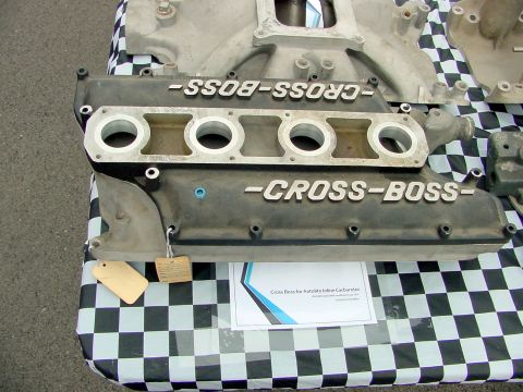 1969 Ford Mustang - A "Cross Boss" intake manifold is displayed on a checkered tablecloth, with a descriptive sign nearby.