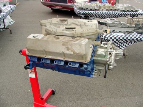 1969 Ford Mustang - Ford V8 engine on a stand, with other engine parts displayed on tables in the background.