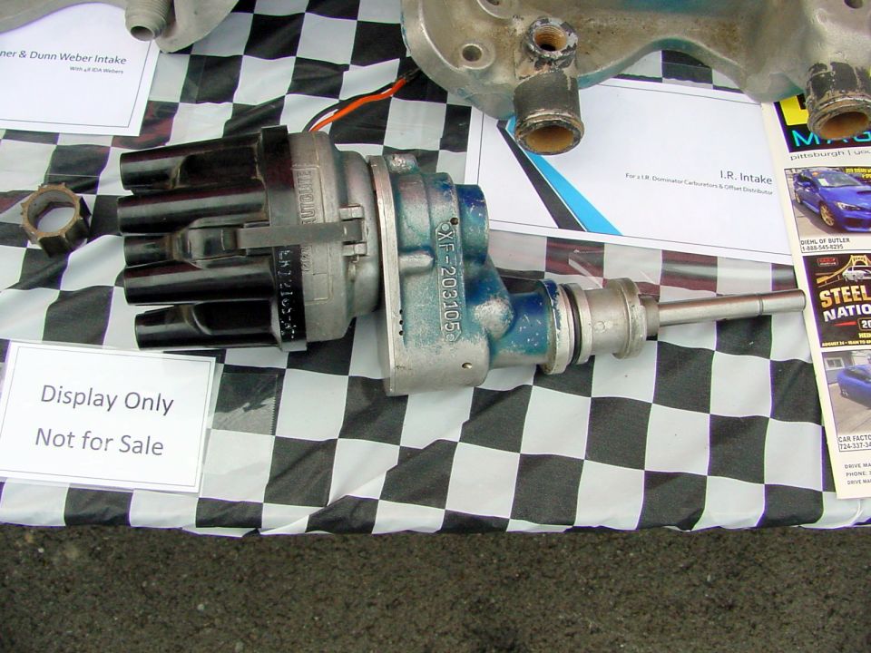 Distributor with wires on checkered cloth, next to intake manifold. Sign says 'Display Only Not for Sale'