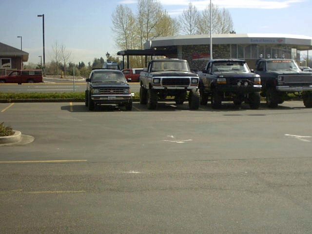 Four dark lifted Ford trucks and an SUV parked nose-out in a bank parking lot
