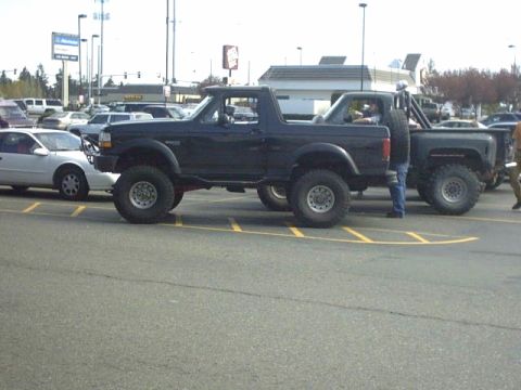 1995 Ford Bronco - Modified 1995 Ford Bronco with off-road tires and spare tire visible in a parking lot.