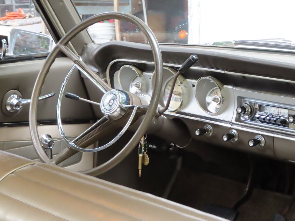Tan interior of a classic Ford with two-spoke steering wheel, round gauges, push-button radio, and keys in ignition.