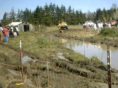 1995 Ford Bronco - Several off-road vehicles are present in a muddy, outdoor setting with spectators observing the scene.