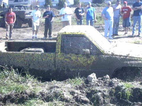 1995 Ford Bronco - A group of men watch as a heavily mud-covered pickup truck is stuck in the mud.