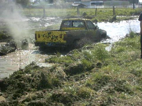 1995 Ford Bronco - Pickup truck struggling through a muddy water obstacle.