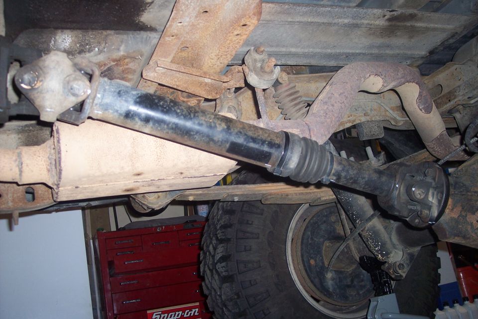 Driveshaft and exhaust system under a vehicle, with a red toolbox visible