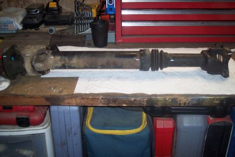 1995 Ford Bronco - A driveshaft, likely removed for repair or replacement, rests on a workbench with various tools and storage bins visible in the background.