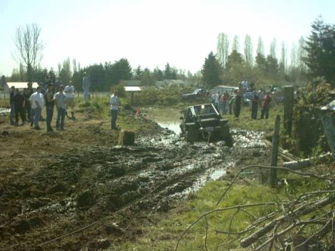 1995 Ford Bronco - A group of people watch as an off-road vehicle struggles in a muddy terrain.