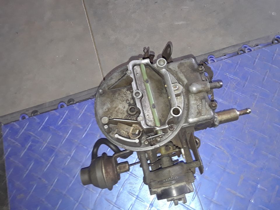 carburetor with vacuum actuator and hoses attached, sitting on a blue textured surface