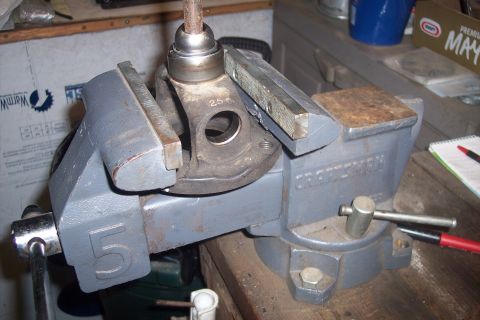1995 Ford Bronco - A driveshaft part is secured in a vise on a wooden workbench, with tools and a notebook nearby.