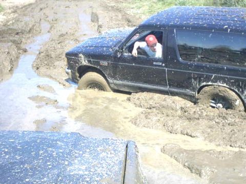 1995 Ford Bronco - A black SUV is deeply stuck in mud, with a person visible behind the wheel.