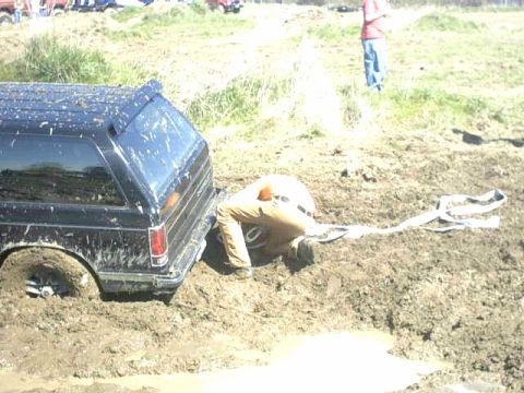1995 Ford Bronco - A person is stuck in the mud next to a black SUV, with a tow strap visible.