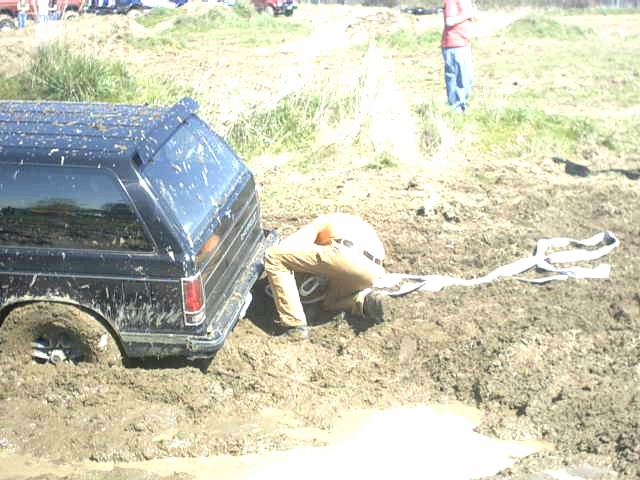 Dark blue Ford Bronco stuck in a mud pit while a person hooks up a recovery strap