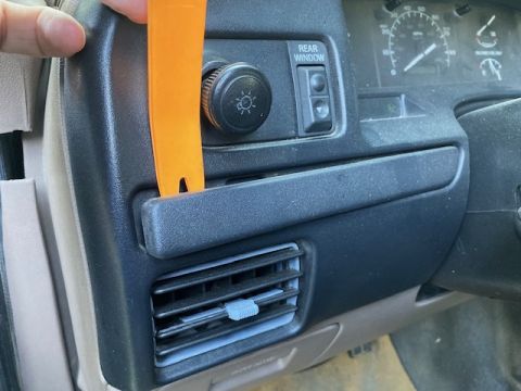 1996 Ford Bronco - A trim removal tool is used to pry a panel on the dashboard of a vehicle.