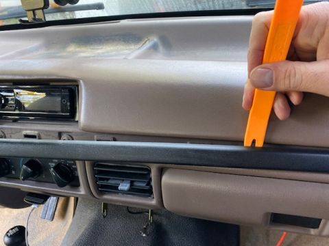 1996 Ford Bronco - A hand uses an orange trim removal tool on the dashboard of a 1996 Ford Bronco.