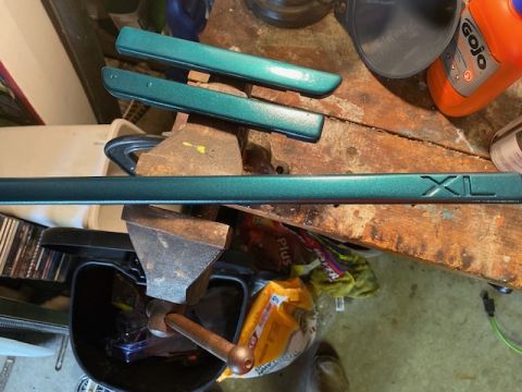 1996 Ford Bronco - Green trim pieces, one with an embossed XL emblem, are clamped in a vise on a workbench.