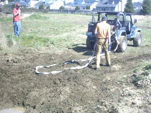 1995 Ford Bronco - A Jeep Wrangler is stuck in the mud, with a tow strap laid out on the ground.