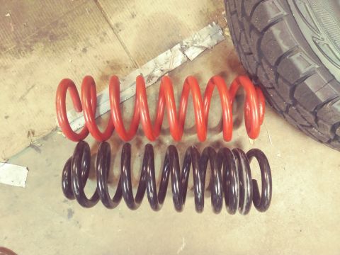 1996 Ford Bronco - A red coil spring and a black coil spring are compared on a garage floor next to a tire.